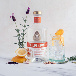bottle of wilderton lustre surrounded by botanicals and a glass with a clear drink
