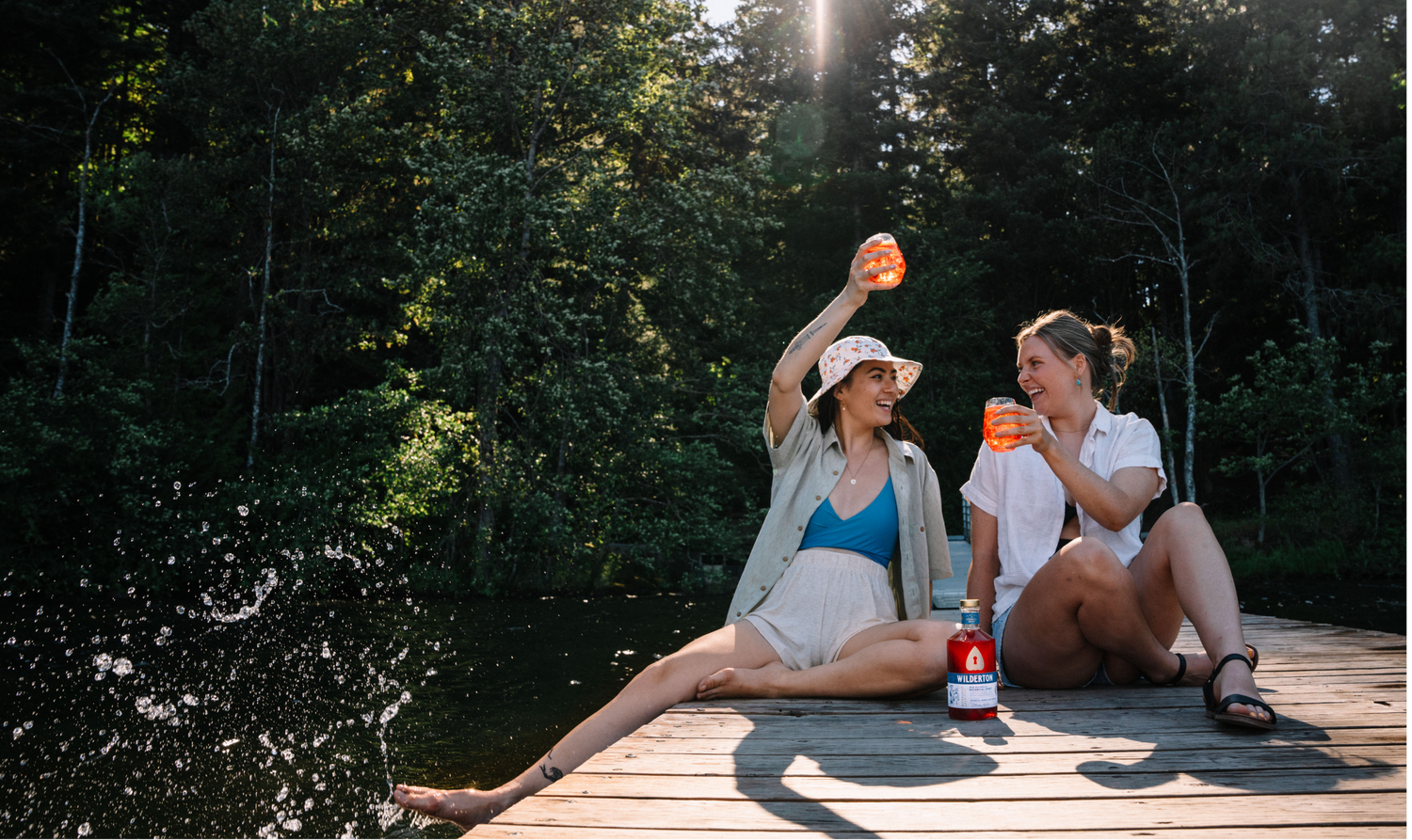 two women sitting on a dock with a bottle of bittersweet aperivito and drinks in hand