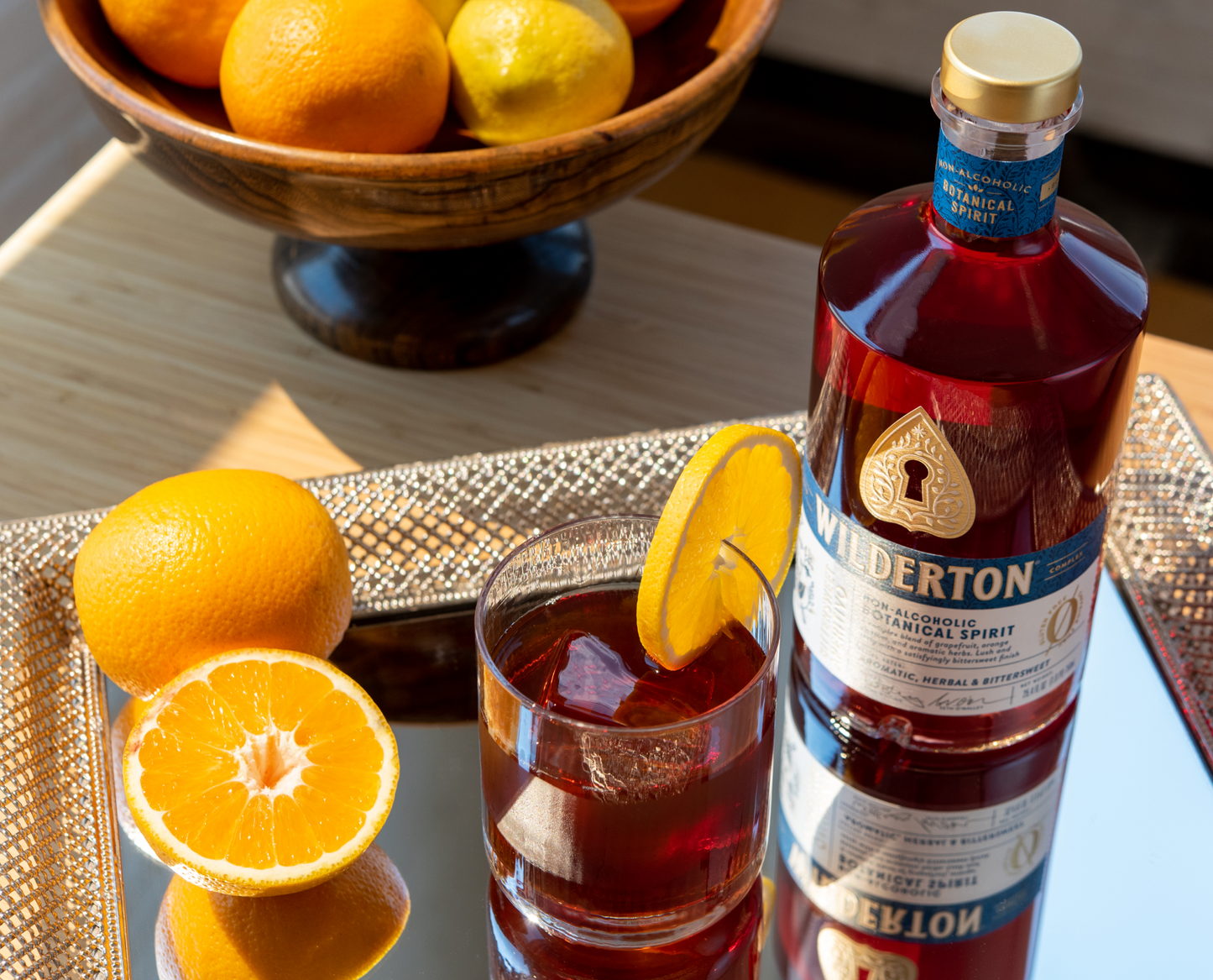 A bottle of bittersweet aperitivo and glass or reddish drink and oranges on a mirror