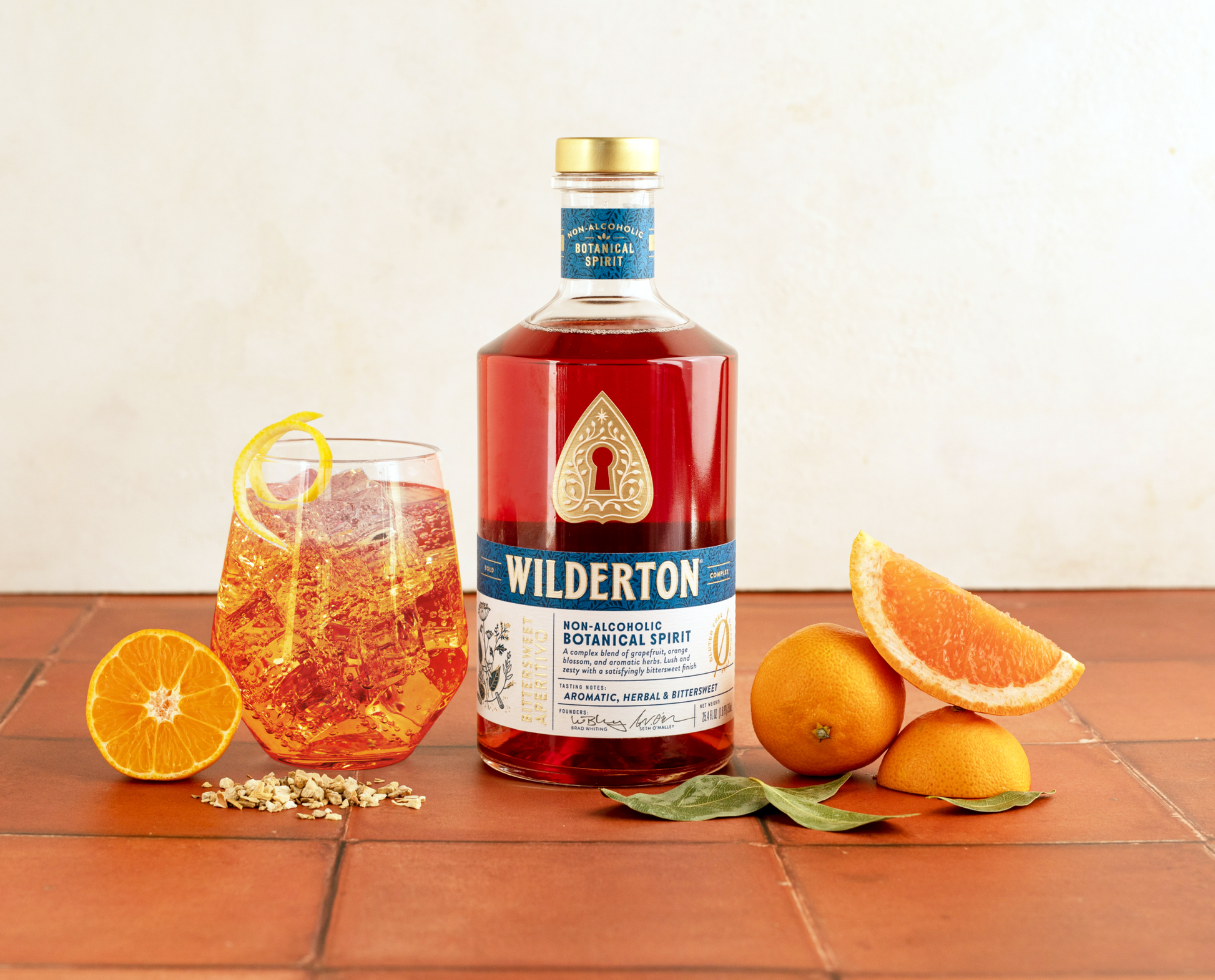 bottles of bittersweet aperitivo next to a glass of wilderton spritz and oranges